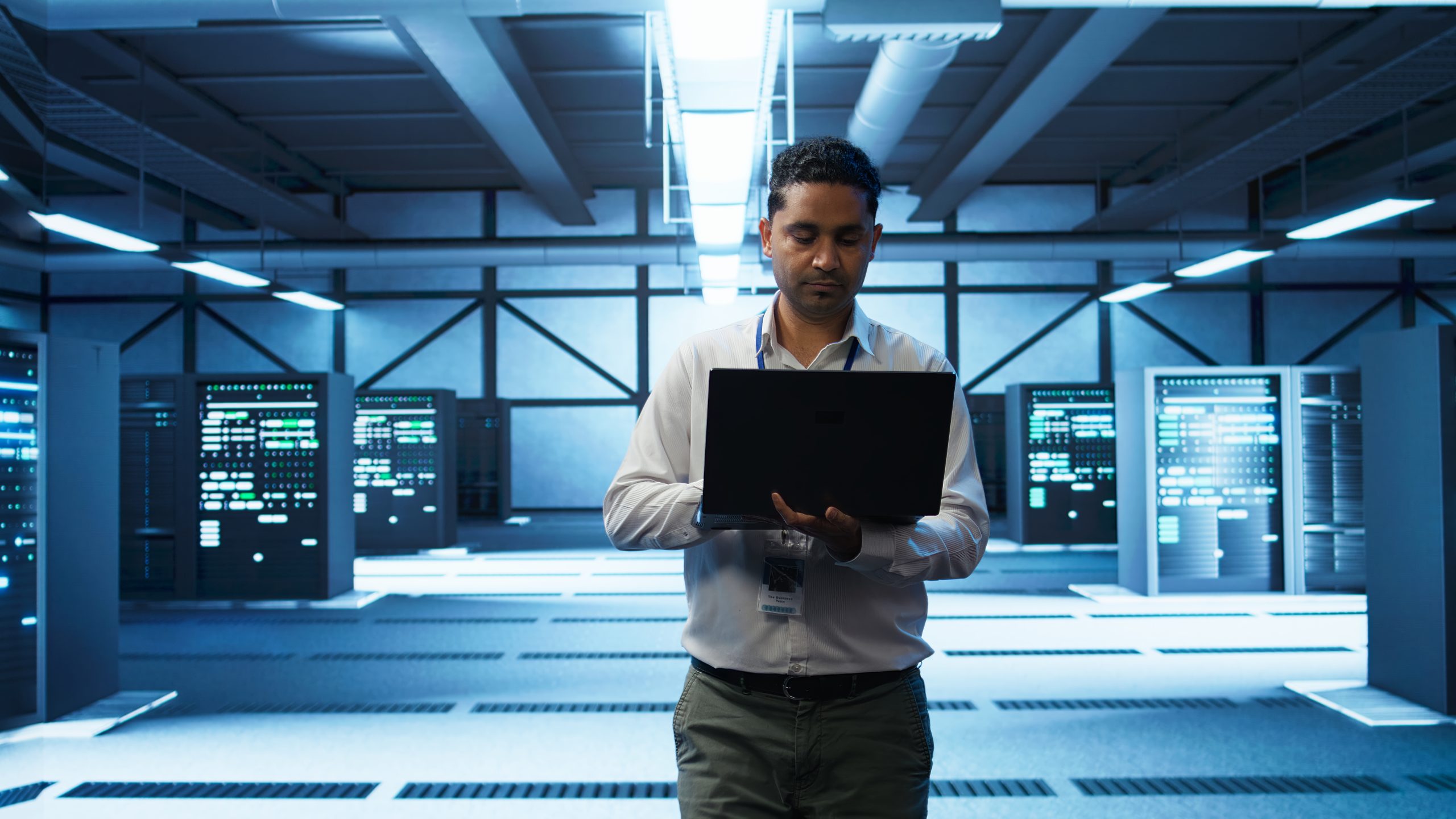 Technician using laptop in data center, managing servers